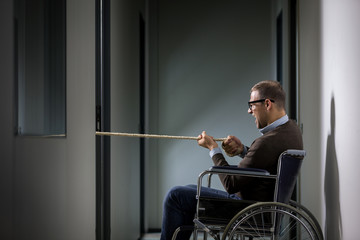 Conceptual photo of man on wheelchair is pulling a rope symboliz
