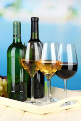 Wine bottles and glasses of wine on tray, on bright background