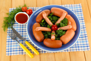 Sausage, greens, tomato on plate on wooden table