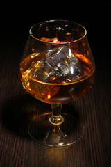 Brandy glass with ice on wooden background