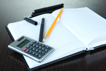 Notebook with pens,pencil and calculator on wooden background