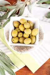 Olives in bowl with branch on napkin on wooden board on table