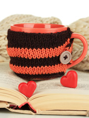 Cup with knitted thing on it and open book close up