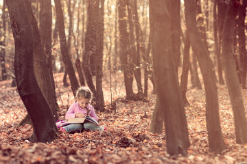 Little girl reading book in autumn forest