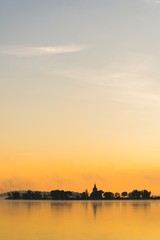 Obraz premium Pionowy minimalistyczny widok wschodu słońca nad jeziorem ze starym kościołem.