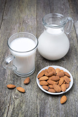 Jug and glass cup with almond milk on a wooden table