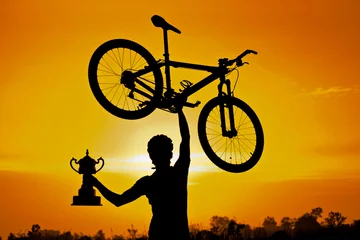 Abwaschbare Fototapete Fahrräder ein Radfahrer, der sein Mountainbike hebt und eine Trophäensilhouette