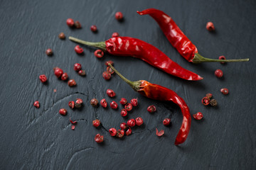 Red chili peppers and red peppercorns, black wooden background