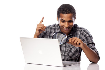 african man looking through a magnifying glass on his laptop