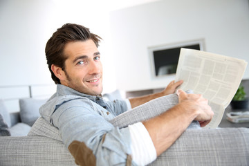 Handsome guy at home reading newspaper