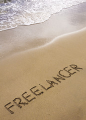 Fototapeta premium Word FREELANCER written in sand, on a beautiful beach