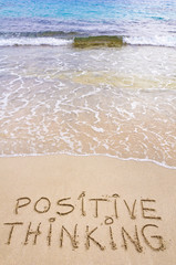 Positive Thinking message written on sand, waves in background