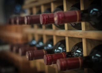 Tuinposter Rode wijnflessen gestapeld op houten rekken © M-Production
