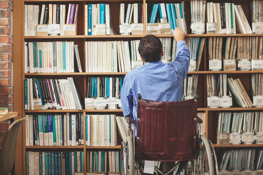 Man in wheelchair taking a book out of bookshelf