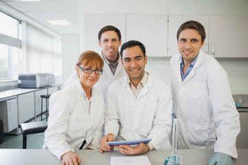 Some scientists standing behind a desk in the laboratory holding a tablet