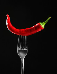 Red hot chili pepper  on fork, isolated on black