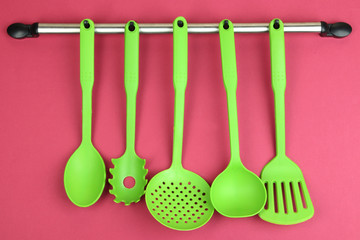 Plastic kitchen utensils on silver hooks on red background