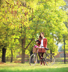 Young female with bicycle in a park reading a book