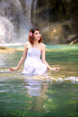 Young woman relaxing in water stream near waterfall