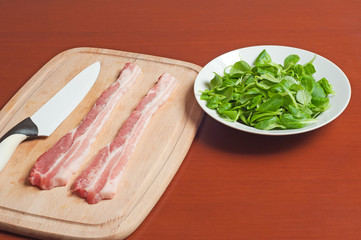 raw bacon and lettuce in a plate on a wooden table and a knife