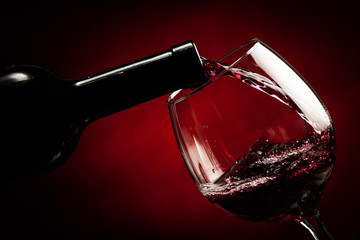 Bottle filling the glass of wine over dark red bacoground - splash of delicious flavor.