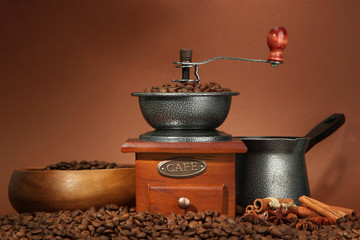 Coffee grinder, turk and coffee beans on brown background