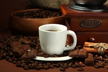 cup of coffee, grinder and coffee beans on brown background