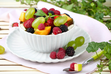 Fruit salad in bowl, on wooden table, on bright background