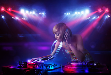 Fototapeta na wymiar Disc jockey girl playing music with light beam effects on stage