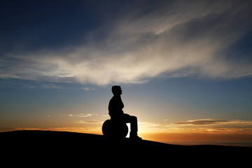 silhouette of man sitting on fitness ball in sunset sky