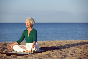 Senior caucasian woman meditating on the beach