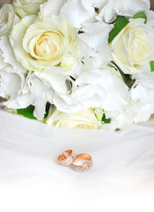Gold wedding rings on a white veil and wedding roses bouquet