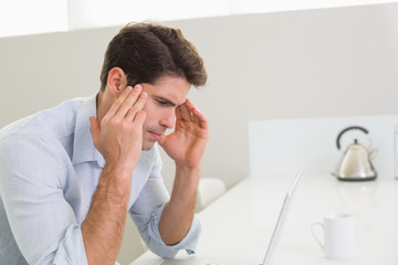 Concentrated casual young man using laptop at home