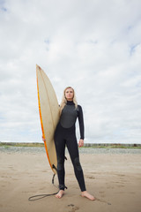 Beautiful woman in wet suit holding surfboard at beach