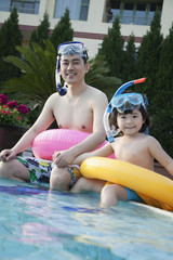 Portrait of father and son in snorkeling gear sitting by the edge of the pool 