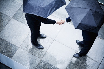 High angle view of two businessmen holding umbrellas and shaking hands in the rain