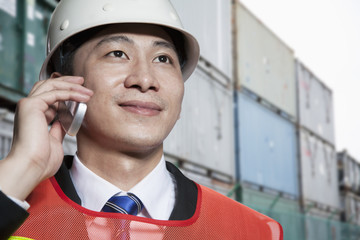 Smiling engineer in protective workwear on the phone in a shipping yard