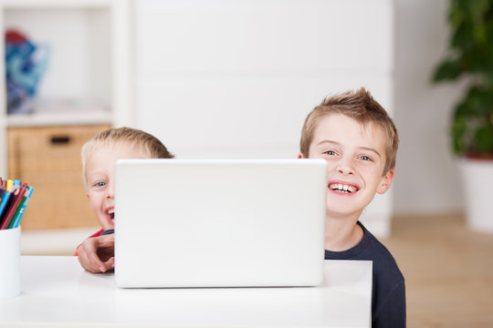 zwei lachende kinder schauen hinter laptop hervor