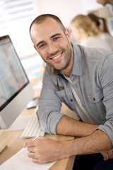 Naklejka na ściany i meble Cheerful guy sitting in front of desktop computer