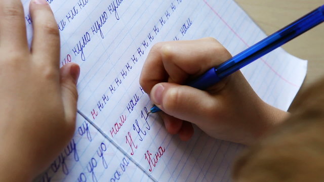 Little boy writes letters in diagonal lined notebook