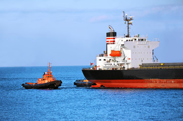 Tugboat assisting bulk cargo ship to harbor quayside