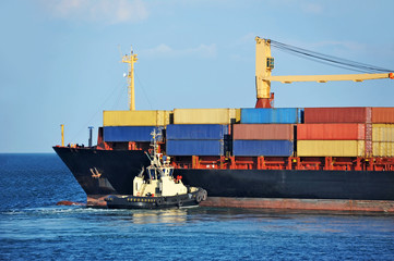Tugboat assisting container cargo ship to harbor quayside