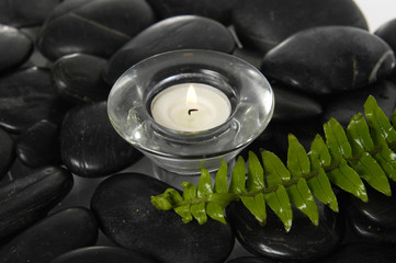 candle in glass with fern on  pebbles