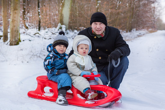 Two little siblings and their father having fun on sledge