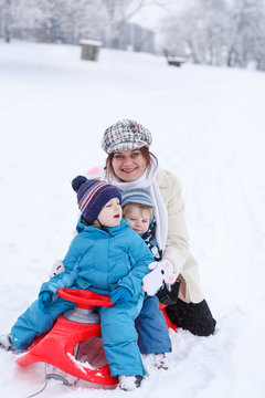 Two little siblings and their mother having fun on sledge on win
