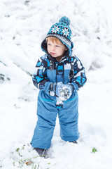 Fototapeta na wymiar Adorable toddler boy having fun with snow on winter day