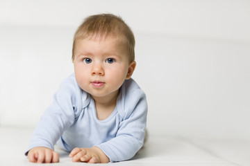 Portrait of adorable baby boy lying on white couch.