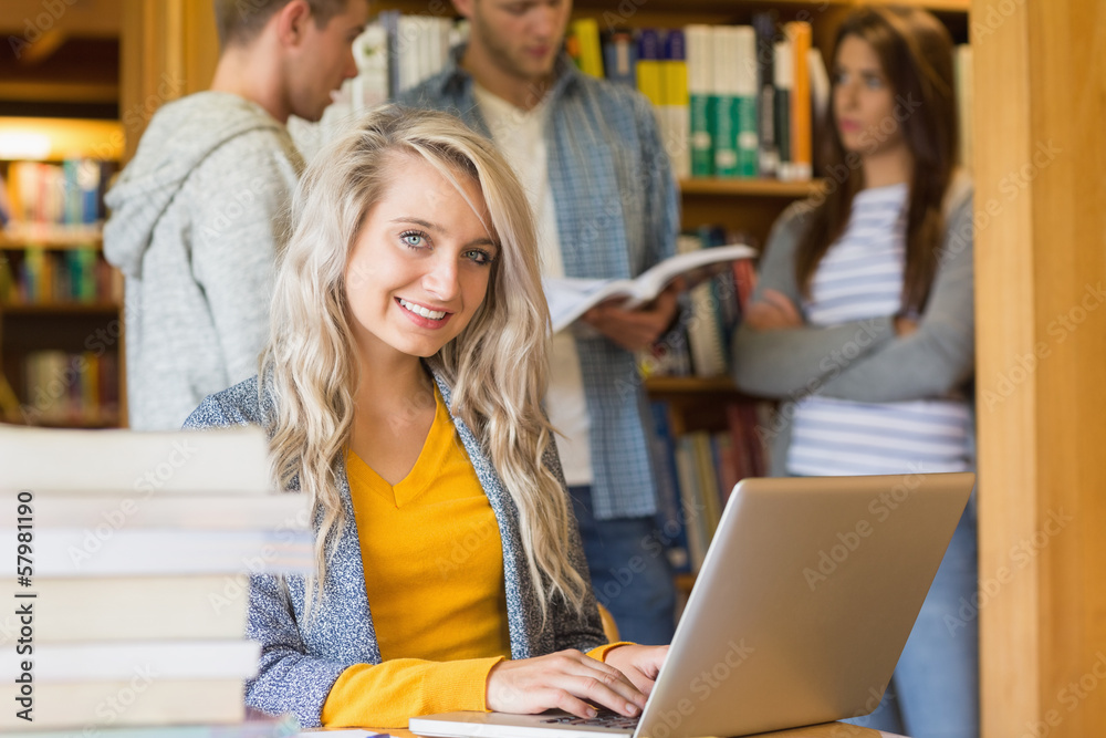 Poster female student using laptop while others in background at librar