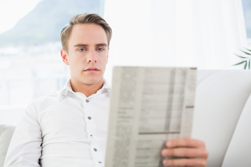 Concentrated relaxed man reading newspaper on sofa