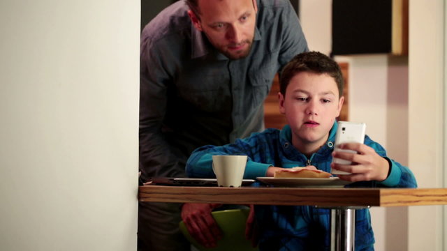 Son showing something on smartphone to his dad during breakfast